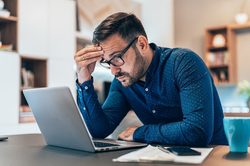worried-man-holding-head-looking-at-laptop-fraud-prevention-ocfo